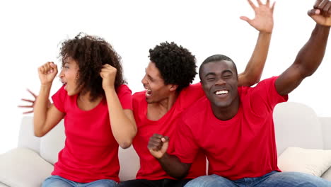 Football-fans-in-red-sitting-on-couch-cheering