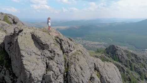 a young woman is standing on the edge of an impressive mountain cliff, dolly zoom