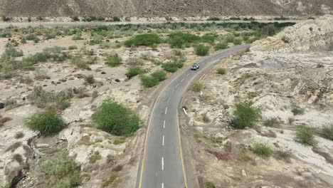 disparo aéreo de avión no tripulado volando sobre un vehículo que conduce a lo largo de la carretera a lo largo de las estribaciones de las montañas en hingol, balochistan, pakistán en un día lluvioso