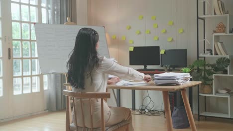 vista trasera de una feliz mujer asiática celebrando el final de trabajo con documentos en la oficina
