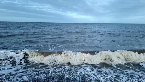 dirty sandy slow motion tide waves crashing onto stormy pebble waterfront looking out across horizon