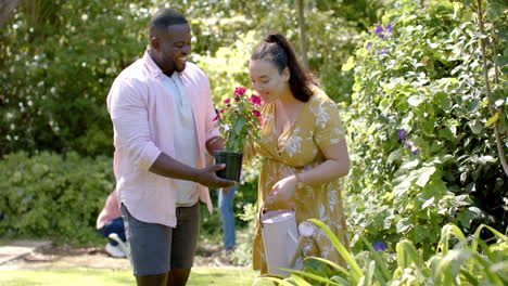 gardening together, african american man holding potted plant, woman with watering can