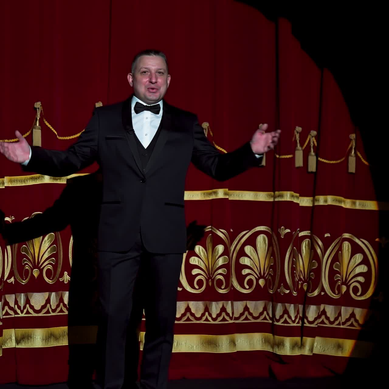 Man is speaking in the light of the floodlights standing on stage to the camera. Actor, artist on performance. Active gestures with hands