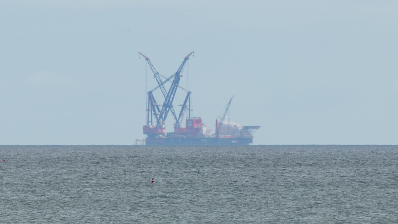 Large industrial barge with cranes travels offshore under overcast daylight, steady camera, wide shot