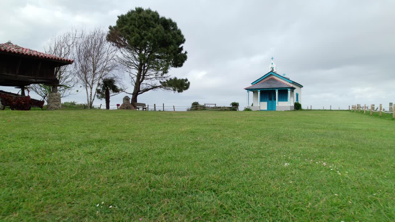 dolly a nivel del suelo de una pequeña iglesia azul y blanca junto a un acantilado hacia el mar, ermita de la regalina, por encima de los acantilados empinados en la costa de asturias, norte de españa