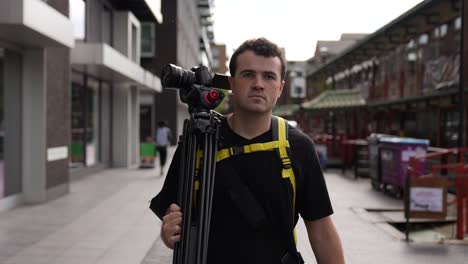 young man is walking the streets of london with his camera on a tripod carrying on his shoulder