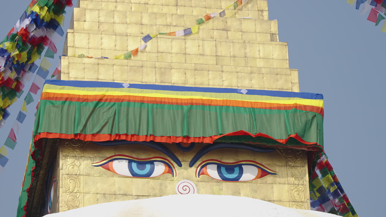 Close-up of Boudhanath Stupa, Kathmandu, Nepal. Sunlight brightens the Buddha eyes while prayer flags flow in the air, symbolizing peace, spirituality, and sacred Buddhist cultural heritage