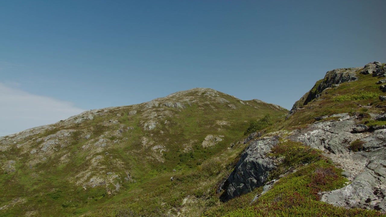 Pendii erbosi e rocciosi del fjell si innalzano verso una cima arrotondata sotto un cielo limpido in una giornata luminosa in Norvegia