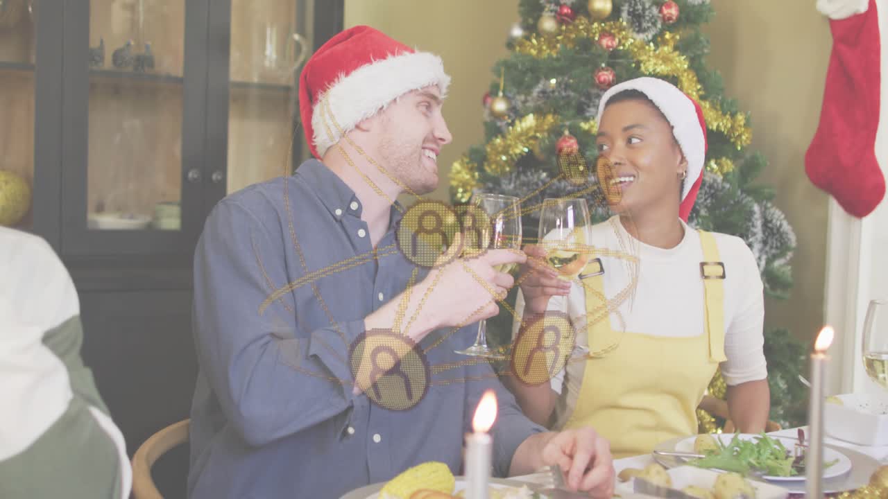 Homem e mulher usando gorros de Papai Noel erguendo taças de vinho em um brinde, celebrando um jantar festivo