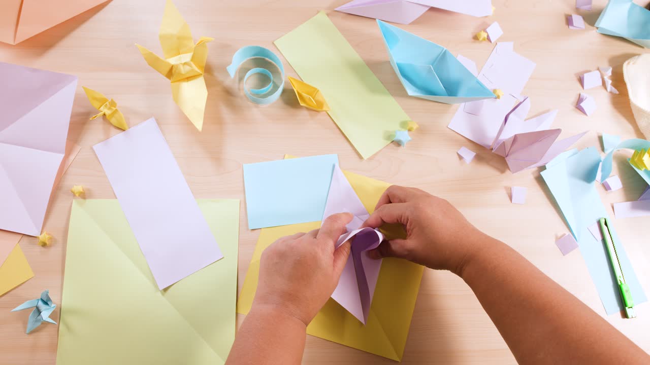 Visuale dall’alto di mani che piegano con precisione un foglio di carta viola per creare un gioco dell’indovino origami