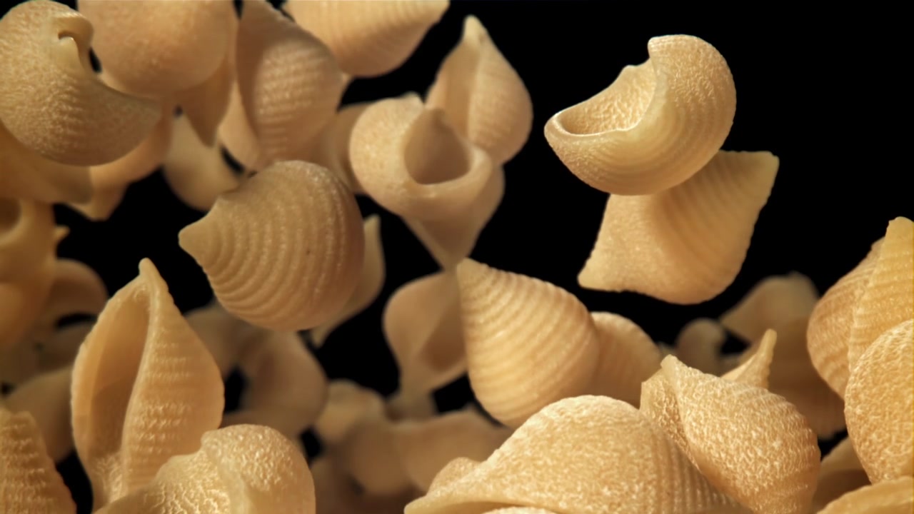 Movimento rallentato di pasta a conchiglia cruda fluttuante su sfondo nero