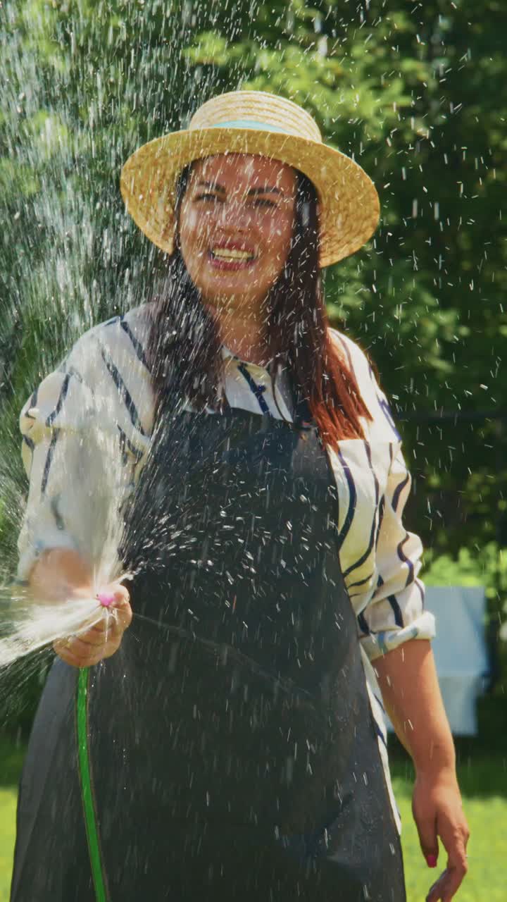 Joyful Gardener in Sunlit Garden Spraying Water - A Woman Embracing Nature and Creating a Refreshing Atmosphere with a Hose During a Warm Day