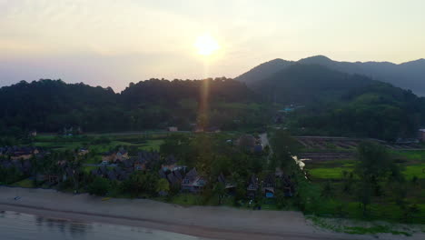 sun rising above hills and bungalow resort on beach in koh chang