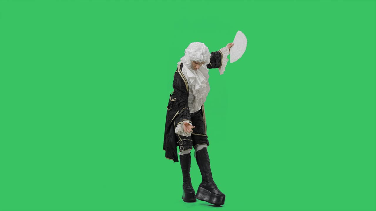 검은색 역사적인 빈티지 슈트와 색 가발을 입은 궁정 신사의 초상화, 팬을 흔들고, 구부리고, 굴복하고, 녹색 스크린 배경으로 스튜디오에서 포즈를 취하는 젊은이.