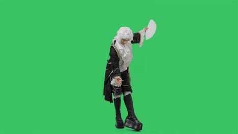 portrait of courtier gentleman in black historical vintage suit and white wig, waving a fan, bowing and curtsy. young man posing in studio with green screen background. full lenght. slow motion