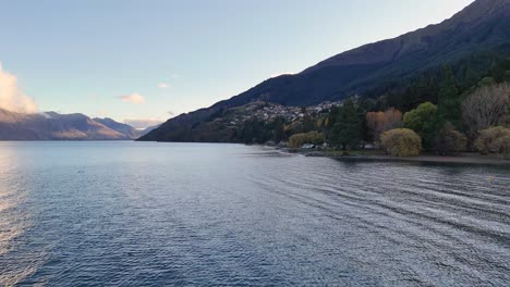 Aerial footage captures serene lake and mountain views in Queenstown, New Zealand, under soft daylight with gentle camera movement