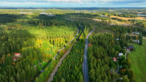 Aerial view following a long cargo train, in middle of sunny, lush green forest