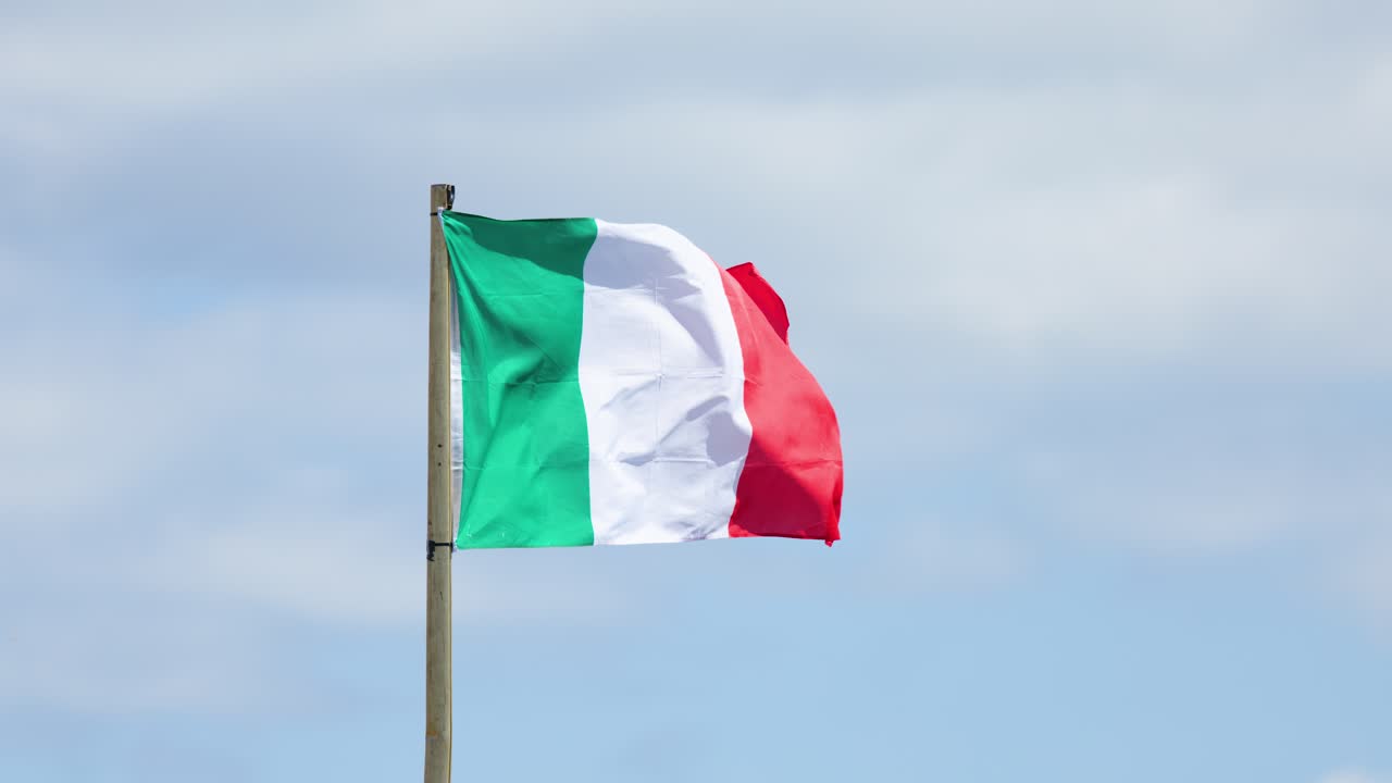 Bandiera italiana che sventola su un pennone con cielo nuvoloso, luce diurna, ripresa stabile, atmosfera da festival all'aperto