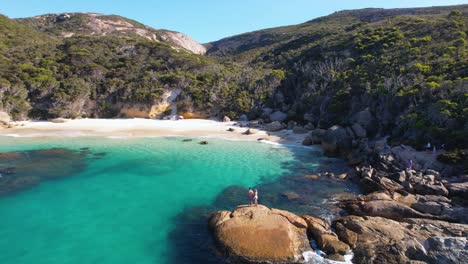 Video-De-Drones-De-4k-Rodeando-A-Una-Pareja-Parada-Sobre-Una-Roca-Mirando-A-La-Playa-De-La-Cascada