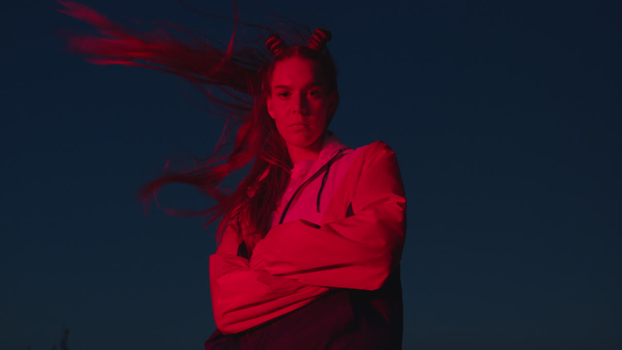 portrait teenage girl posing in city at night looking confident with urban style in red light wind blowing hair