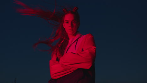 portrait-teenage-girl-posing-in-city-at-night-looking-confident-with-urban-style-in-red-light-wind-blowing-hair