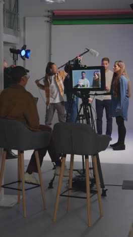 vertical video of female assistant using clapperboard as actors shoot movie or video in studio with film crew and director shot in real time 1