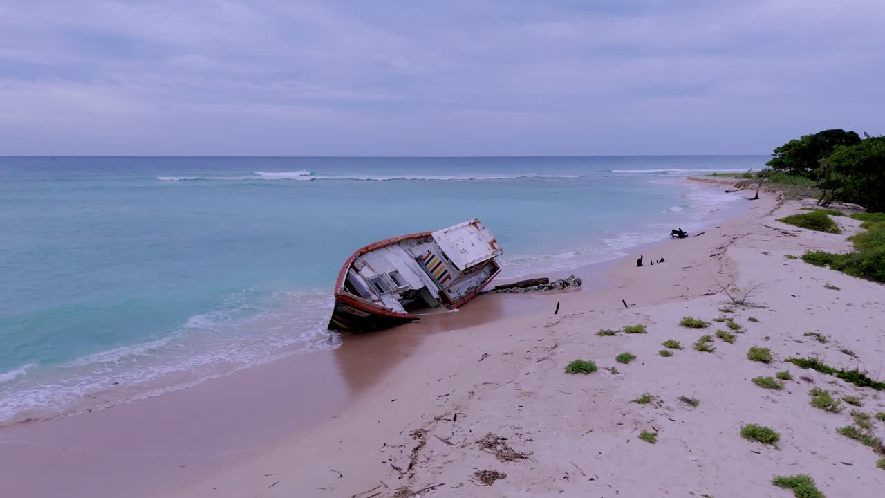 Fishing boat on sand bank with lashing aqua green blue waves. Bay of Bengal sea, Sri Lanka. Drone fly over.