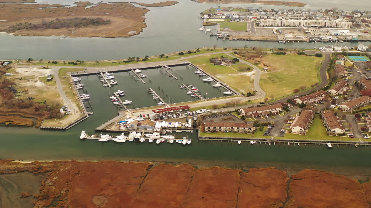 A high angle drone view over a salt marsh with a square dock in view. The camera dollys in and tilts down towards the docks - the calm waters below. It's a cloudy day and it is quiet.