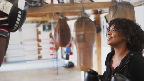 male boxing coach with female boxer in gym using training gloves