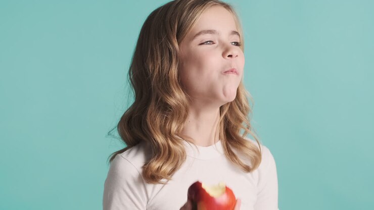 Teenage Caucasian girl in pijamas eating an apple and smiling.