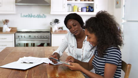 mother helps teenage daughter with homework using digital tablet