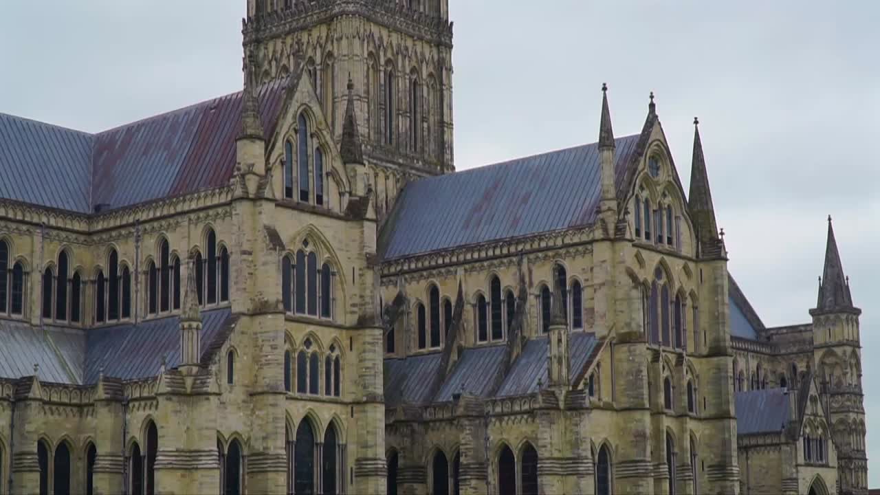 Detailed static shot capturing the intricate Gothic architecture and weathered stonework of Salisbury Cathedral’s upper structure in Wiltshire, southern England.
