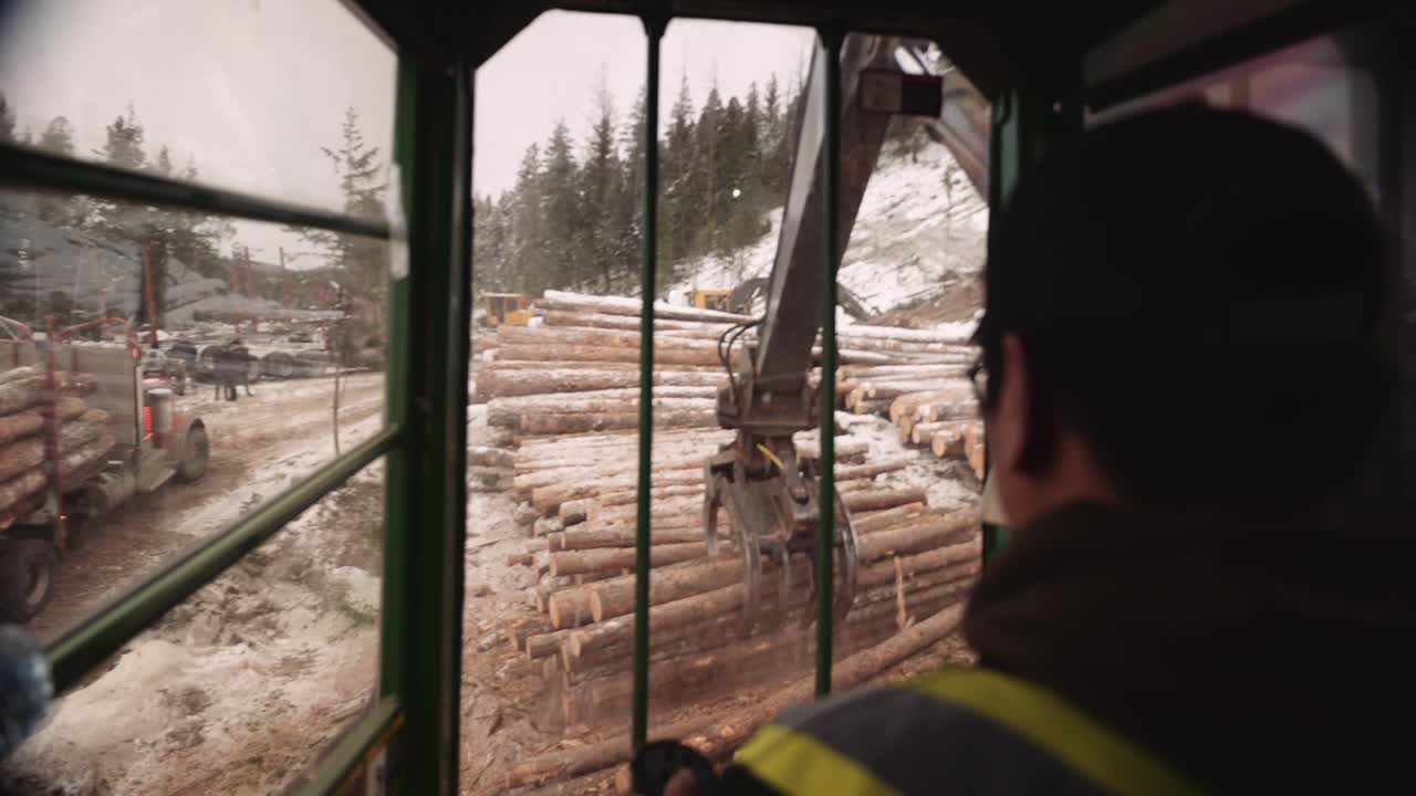 First person POV blue collar tradesman operates industrial timber logging manipulator arm claw tractor from inside cabin with joystick