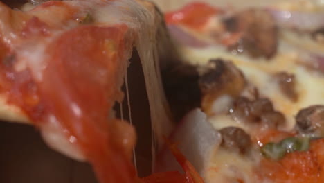 recogiendo una rebanada de pizza fresca con el queso derretido estirándose mientras las piezas se separan - cierre aislado