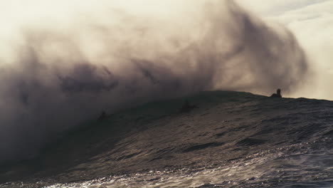 barrel of wave crashes collapsing and spitting out mist over surfers