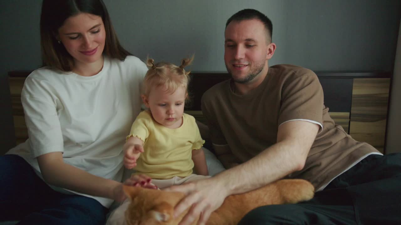 Famiglia felice con bambino e gatto rosso che si coccolano sul letto