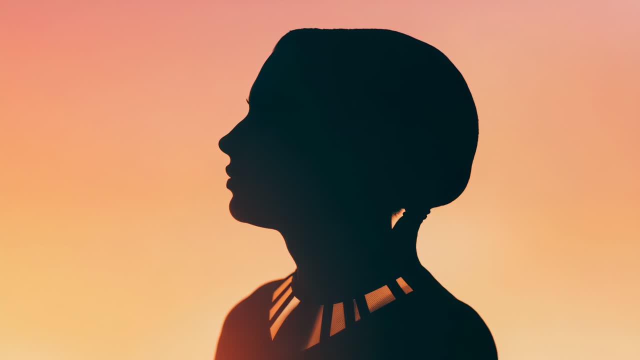 Warm rim light brightening woman darkening into silhouette in studio, showing dark top and necklace