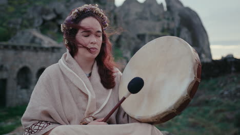 Mujer-Espiritual-Tocando-Un-Tambor-Chamánico-En-Un-Hermoso-Pueblo-Medieval-Plano-Medio