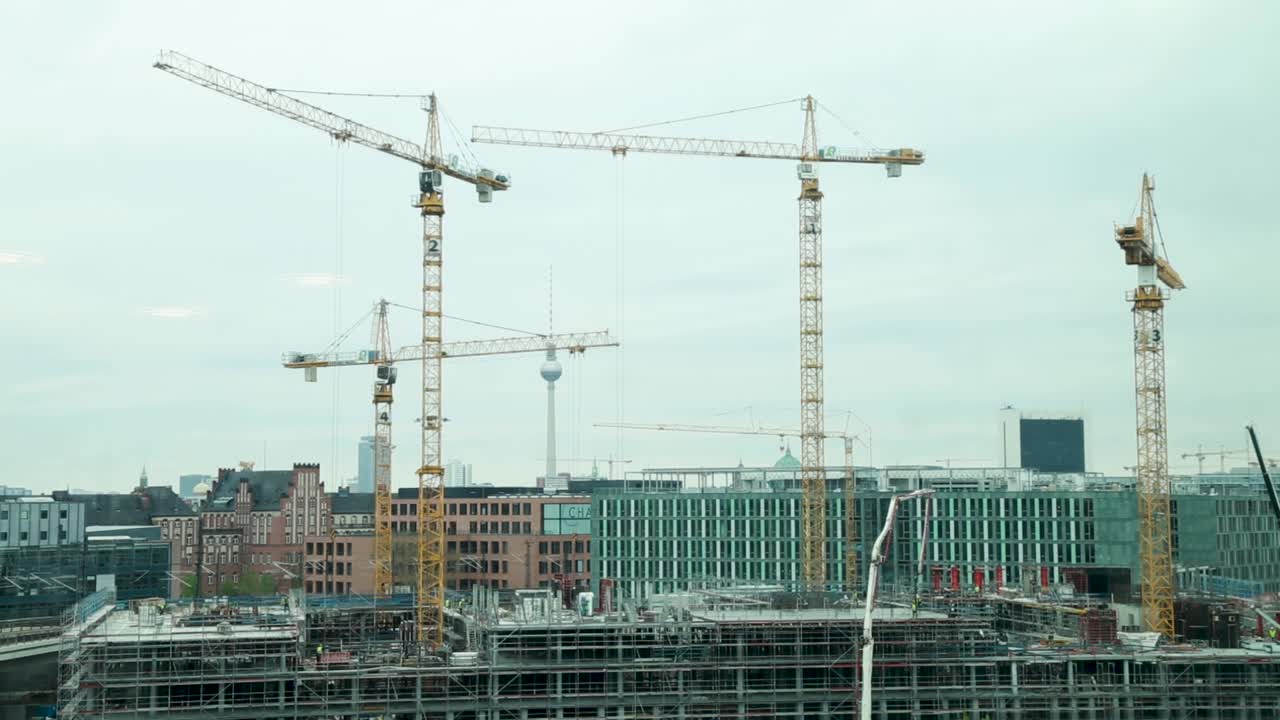 Construction cranes towering over a building site in Berlin with the iconic TV Tower in the background
