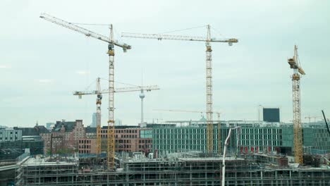 construction cranes towering over a building site in berlin with the iconic tv tower in the background