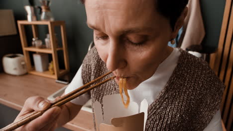 person eating noodles from a takeaway box with chopsticks