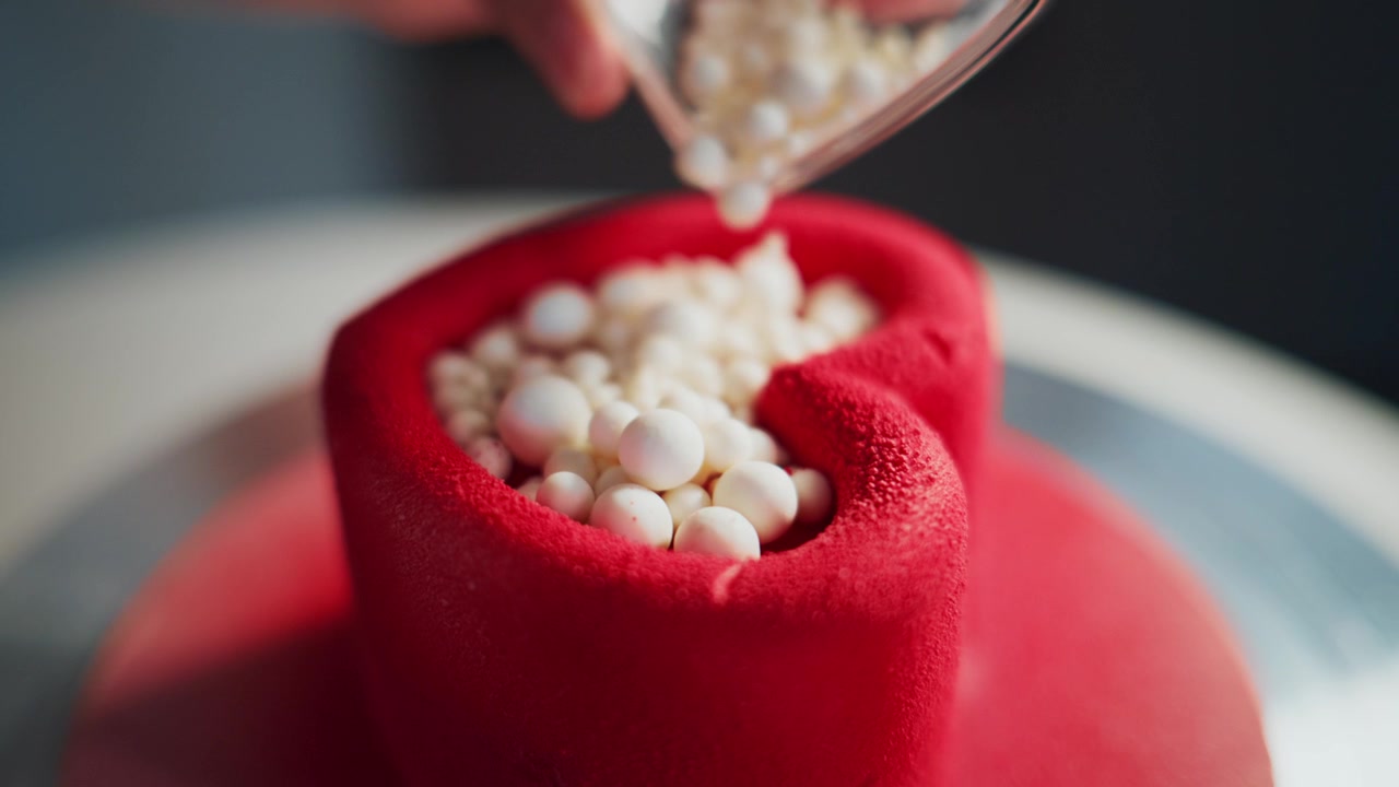 Una mano versa perle di zucchero bianche su una torta di pasta di zucchero rossa. Il movimento fluido si concentra sul processo di decorazione dolce. Perfetto per pubblicità di dolci, tutorial di pasticceria o temi festivi.