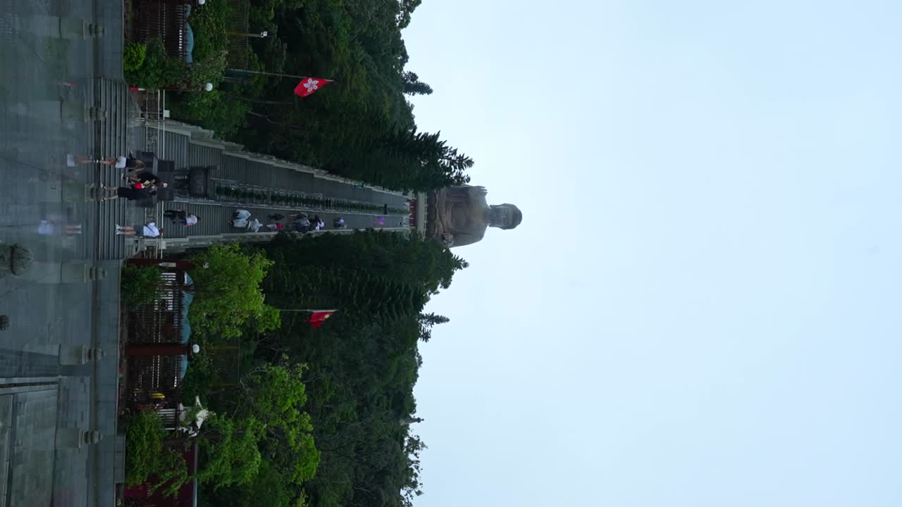 Tourists reflected on ground after rain, climbing towards Tian Tan Buddha, Hong Kong. Vertical