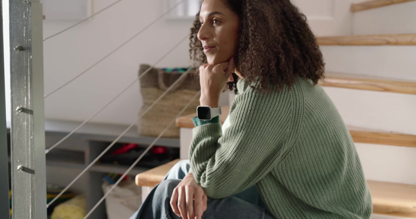 African American adult woman in green knit tapping phone prompted by phone on stairs, reading texts