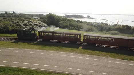 Old-steam-engine-train-riding-next-to-a-lake-in-Netherlands,-Brouwersdam