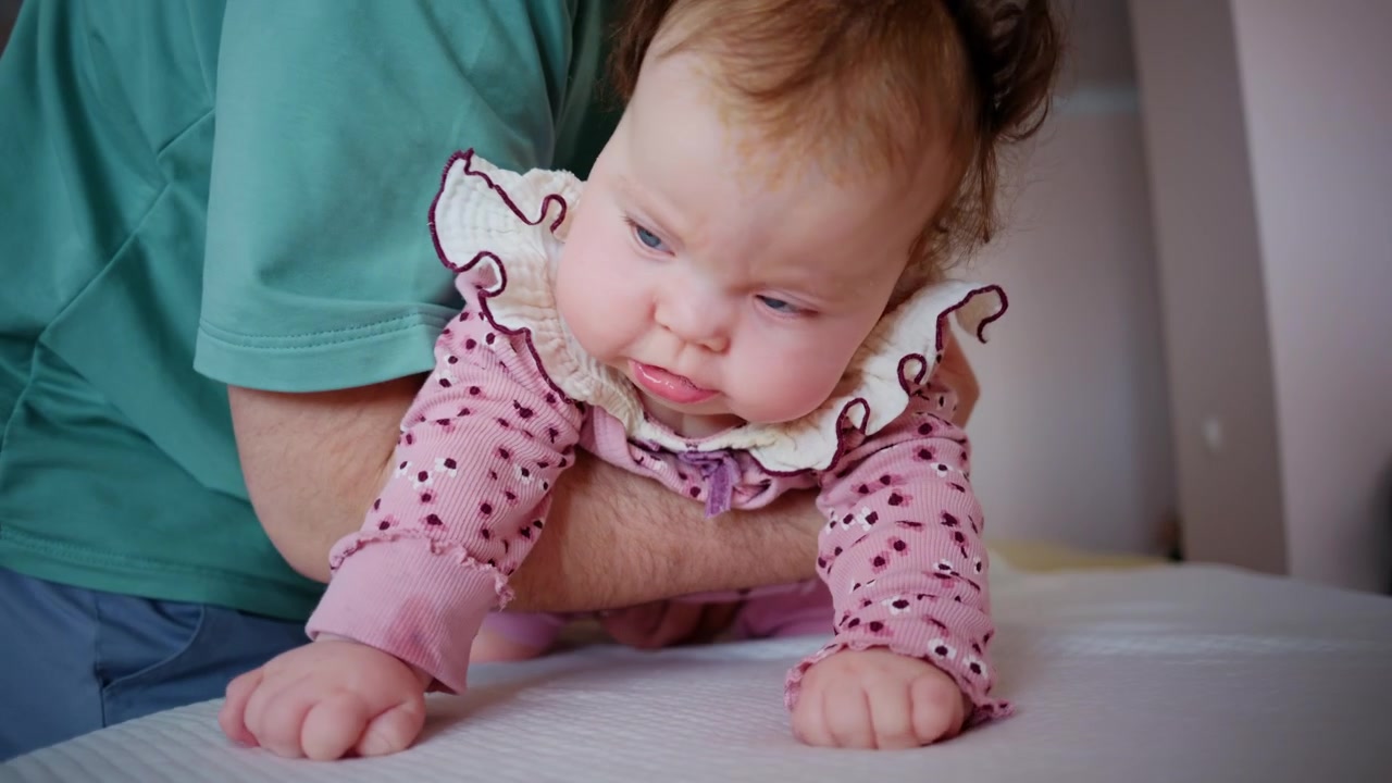 Baby being gently supported by an adult during a tummy time exercise on a padded treatment table