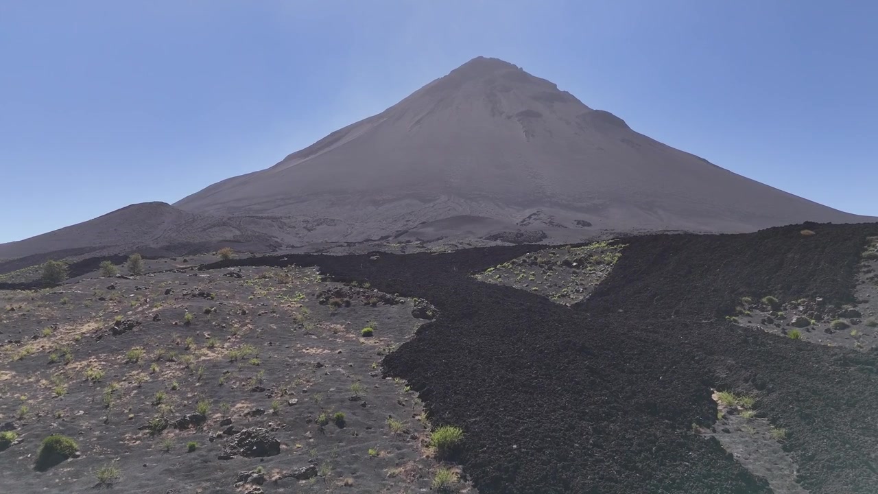 Drone aereo di sentieri di lava solidificata su terreno vulcanico scuro che conducono verso la base del Pico do Fogo nella regione di Chã das Caldeiras, Capo Verde