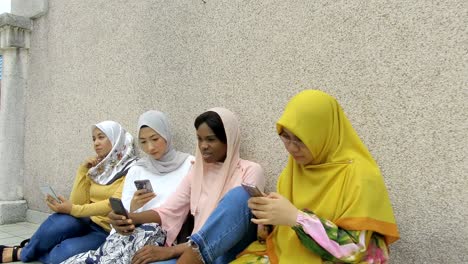 university students in hijab using smartphone in college with friends