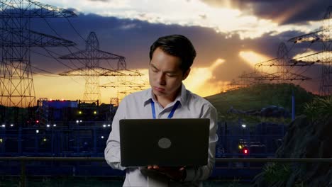 asian male professional worker standing with his laptop near high voltage tower, industrial facility, he is nodding his head with dissapionted