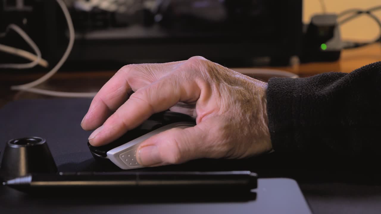 la mano de un hombre mayor usando un ratón de computadora en una mesa en casa